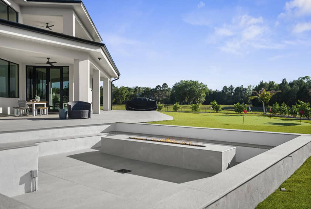 A backyard poolside scene with a clean white patio and a contemporary home in the background under a clear sky.