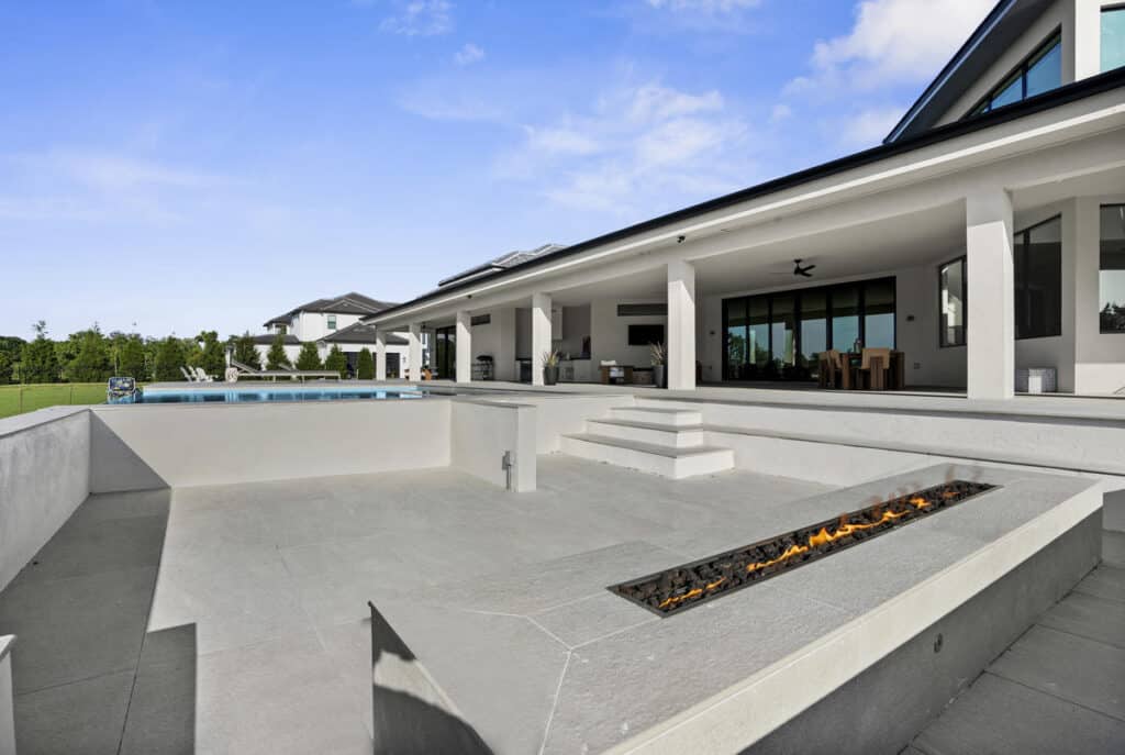 A clean, spacious patio with built-in fire pit and a modern home exterior, leading to a backyard area.