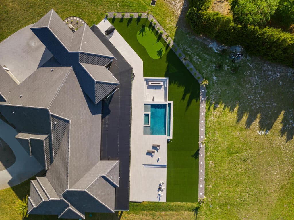A drone’s eye view of a sprawling backyard with a pool, green lawns, and modern home structures, under a sunny sky.