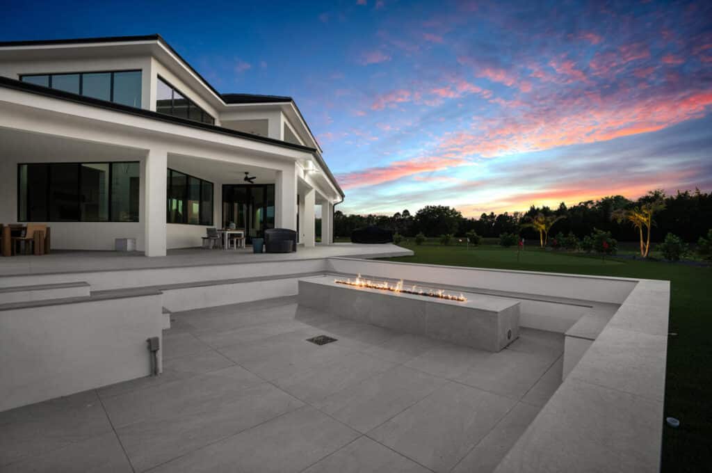 A luxurious backyard pool at dusk, with the calm water reflecting a vibrant sunset and surrounded by modern landscaping.