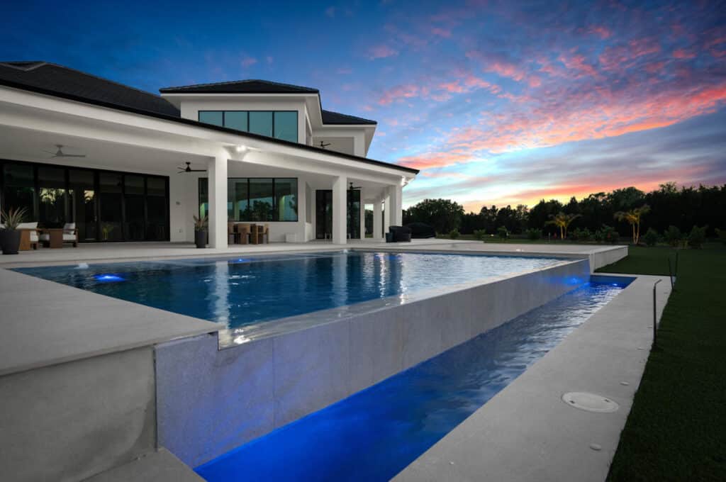 A luxurious backyard with a pristine pool at dusk, reflecting the colors of the sunset and framed by modern architecture.