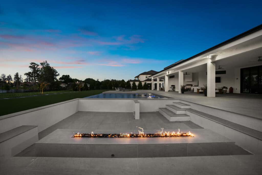 A modern backyard pool glowing in the light of dusk, with smooth concrete decking and a hint of warm-colored lights.