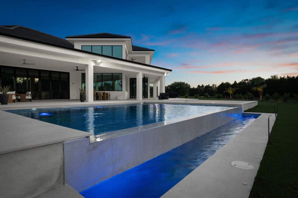 A modern backyard contemporary pool reflecting the soft colors of dusk, with surrounding contemporary landscaping.