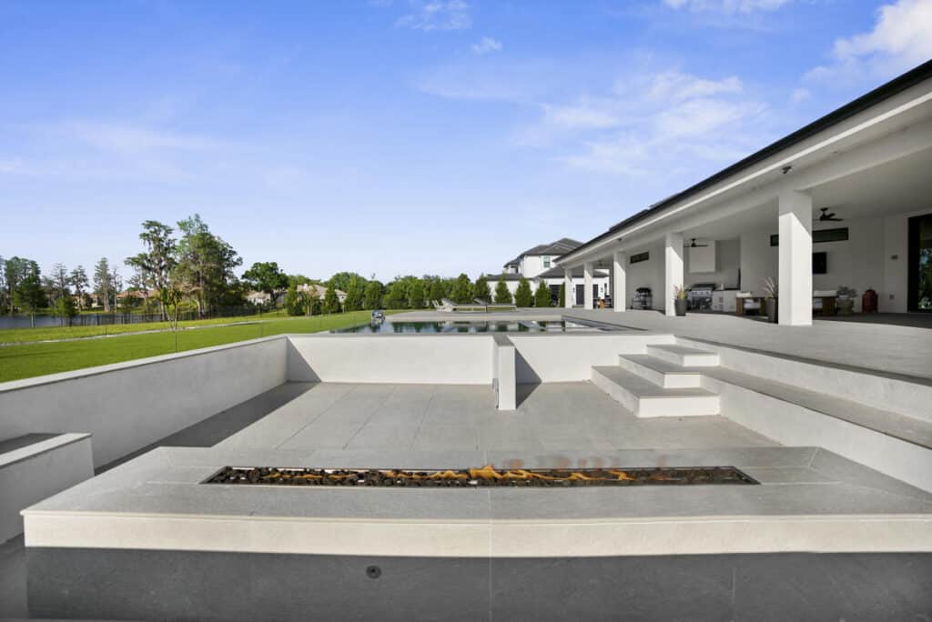 A modern outdoor seating area with a rectangular fire feature, overlooking a backyard pool and lawn.