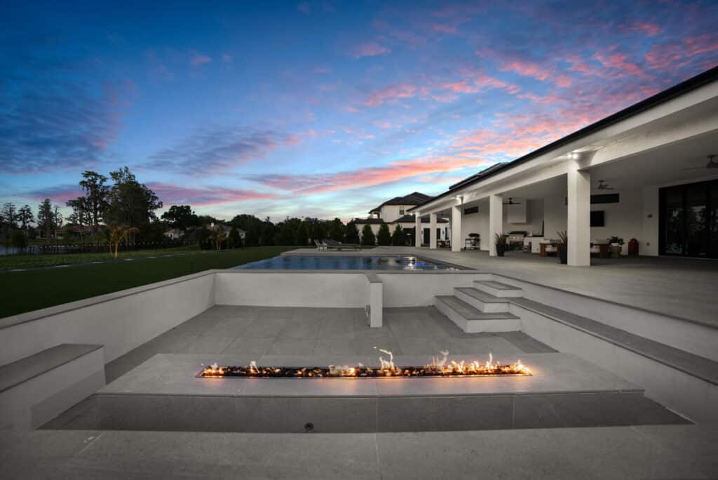 A modern pool reflecting the sunset’s pink and orange hues, with surrounding white tiles and contemporary landscaping.