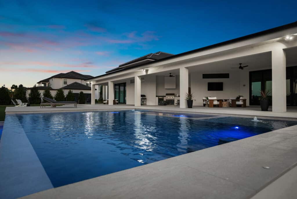 A pool reflecting the evening sky, framed by clean patio tiles and minimalistic landscaping design.