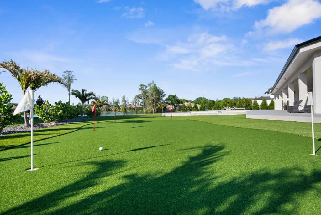 A private backyard putting green surrounded by palm trees and open sky, perfect for practice and leisure.