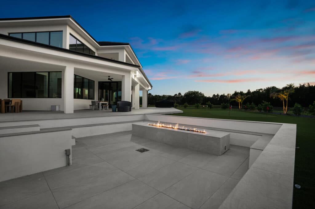A sleek backyard fire pit set in a modern patio, with a contemporary home and glowing sunset sky in the background.