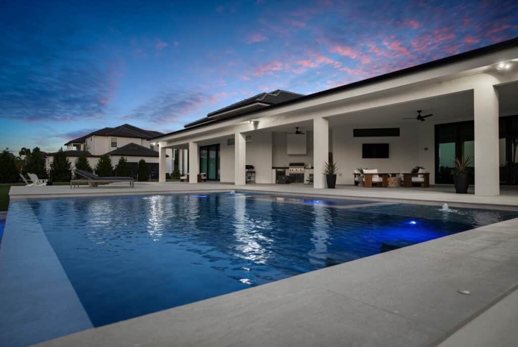 A stylish modern pool at twilight with a smooth concrete pool deck, reflecting the colors of the sunset and framed by a contemporary home.