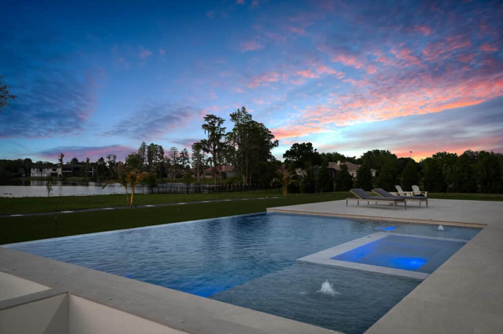 A twilight sky filled with soft pink and purple clouds above a tranquil pool surrounded by greenery and modern design elements.