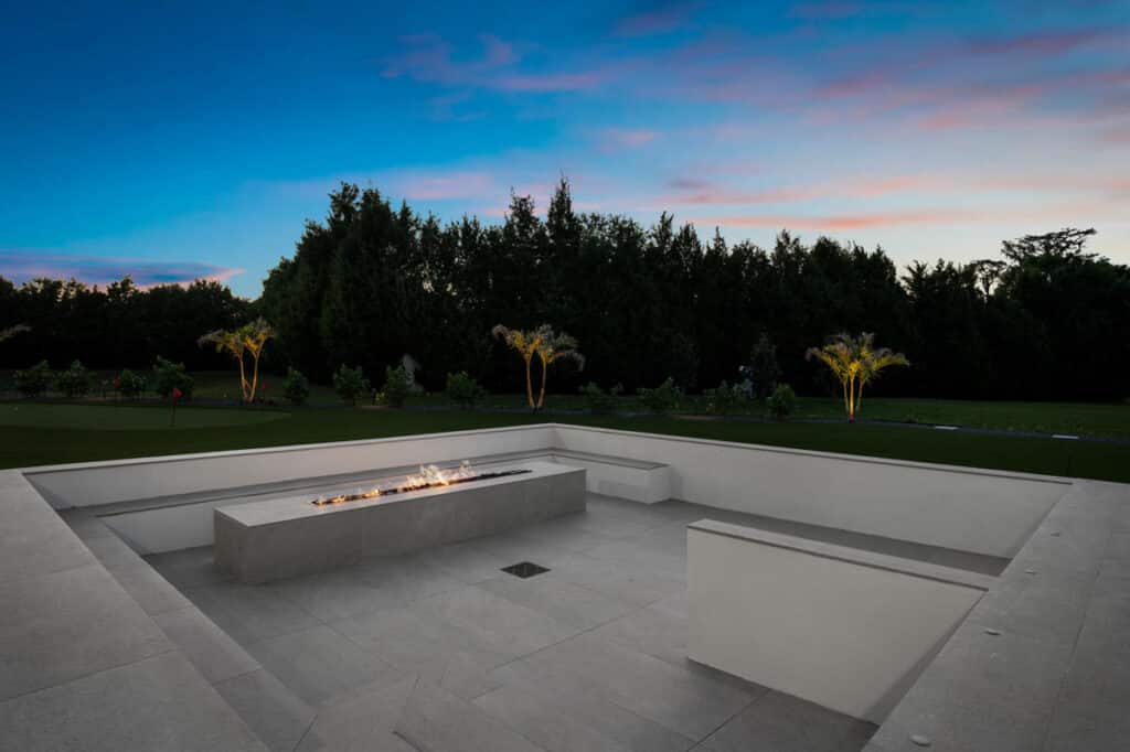 A warm backyard setting with a glowing fire pit, surrounded by modern seating and lush landscaping.